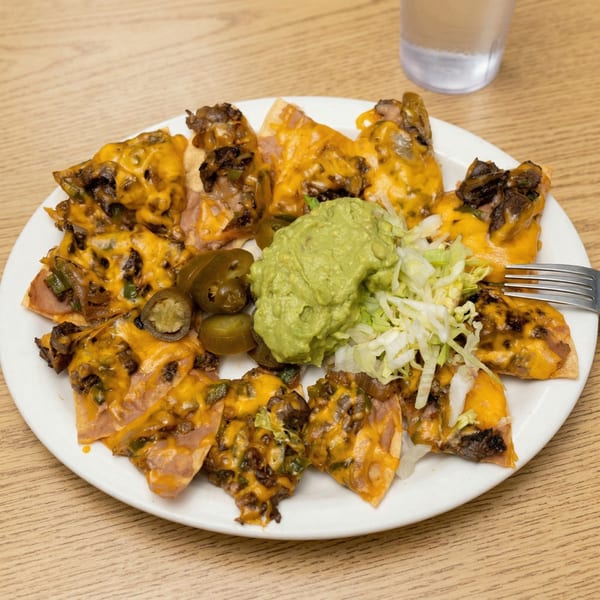 A plate of nachos with melted cheese, meat, jalapeños, guacamole, and shredded lettuce.