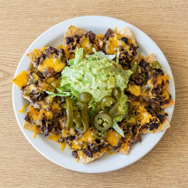 Overhead view of a plate of nachos with melted cheese, meat, guacamole, lettuce, and jalapeños.