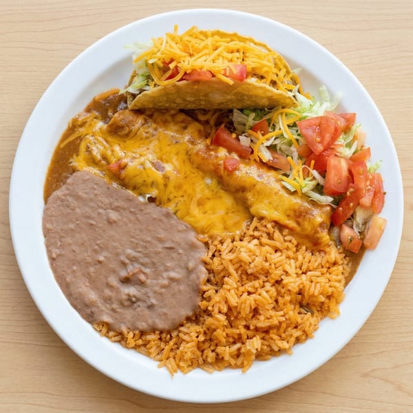 A white plate holds a Mexican combination platter with a taco, enchiladas, refried beans, and rice.