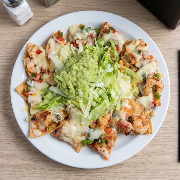 Shrimp nachos with melted cheese, diced vegetables, shredded lettuce, and a dollop of guacamole.