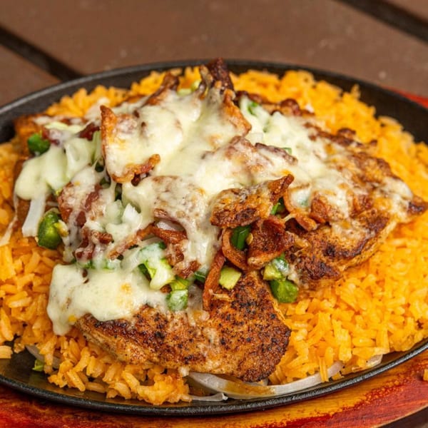 Sizzling Mexican dish with grilled chicken, melted cheese, peppers, onions, and orange rice in a black skillet.